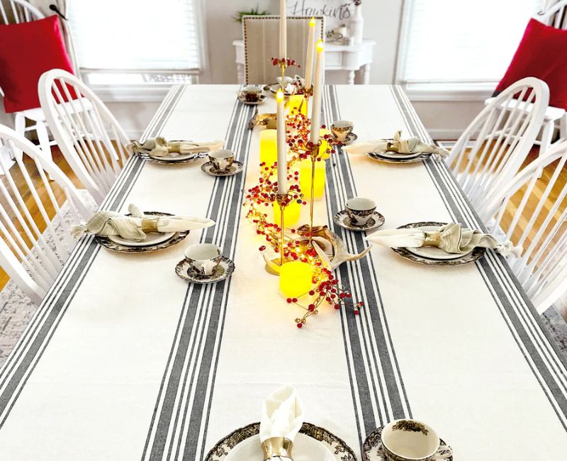 A dining table set with a striped tablecloth featuring a red border. The tablecloth has alternating stripes, with a solid red border around the edges. 