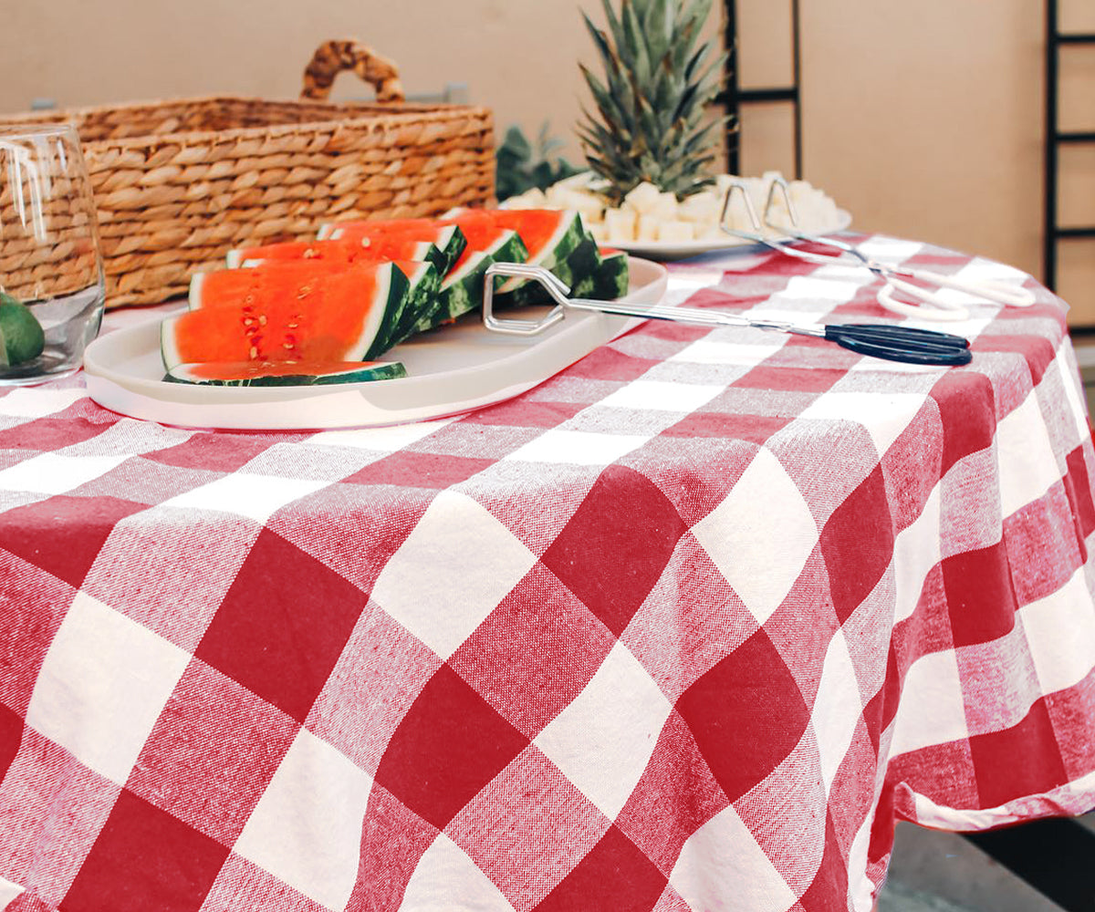 Rustic dining setting with a red cotton tablecloth, wooden chairs, and a vase of sunflowers.