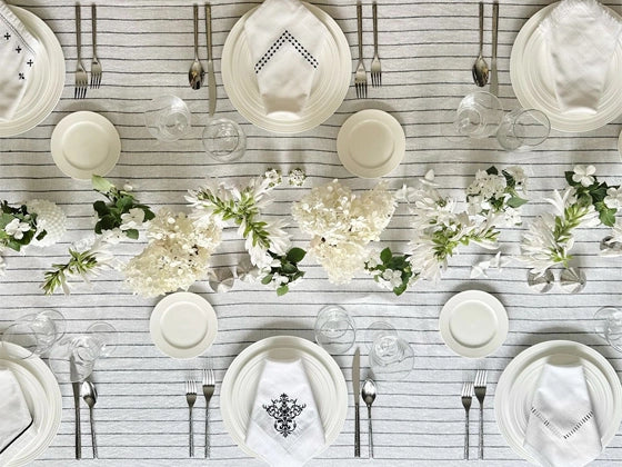 Assorted napkins including linen, embroidered, plaid, striped, and hemstitched designs arranged on a table.