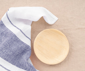 Wooden plate with a Belgian-striped towel on beige linen.