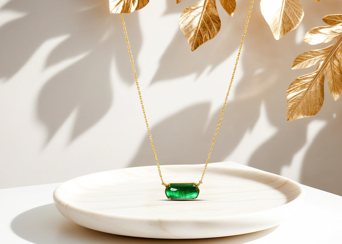 A chunky gold necklace with a emerald green pendant.