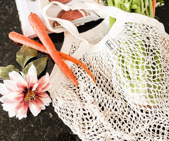 Carrots and mixed vegetables visible in a white cotton mesh bag