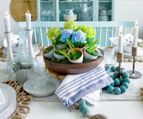 Table setting with blue country striped napkins, a floral centerpiece, candles, and glassware.