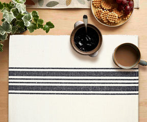 Table setting with a striped white placemat, jam, coffee, waffles, and grapes.