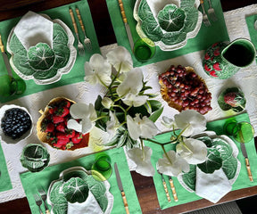 Table setting with Hermstitched ivory napkins, green plates, fresh fruits, and white orchids.