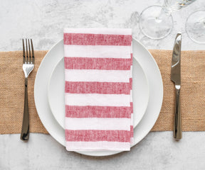 Striped linen napkins in subtle floral designs, folded beside glassware on a well-lit dining table.