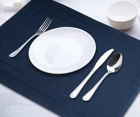 White plate and silver cutlery on a navy blue linen placemat with simple stitching