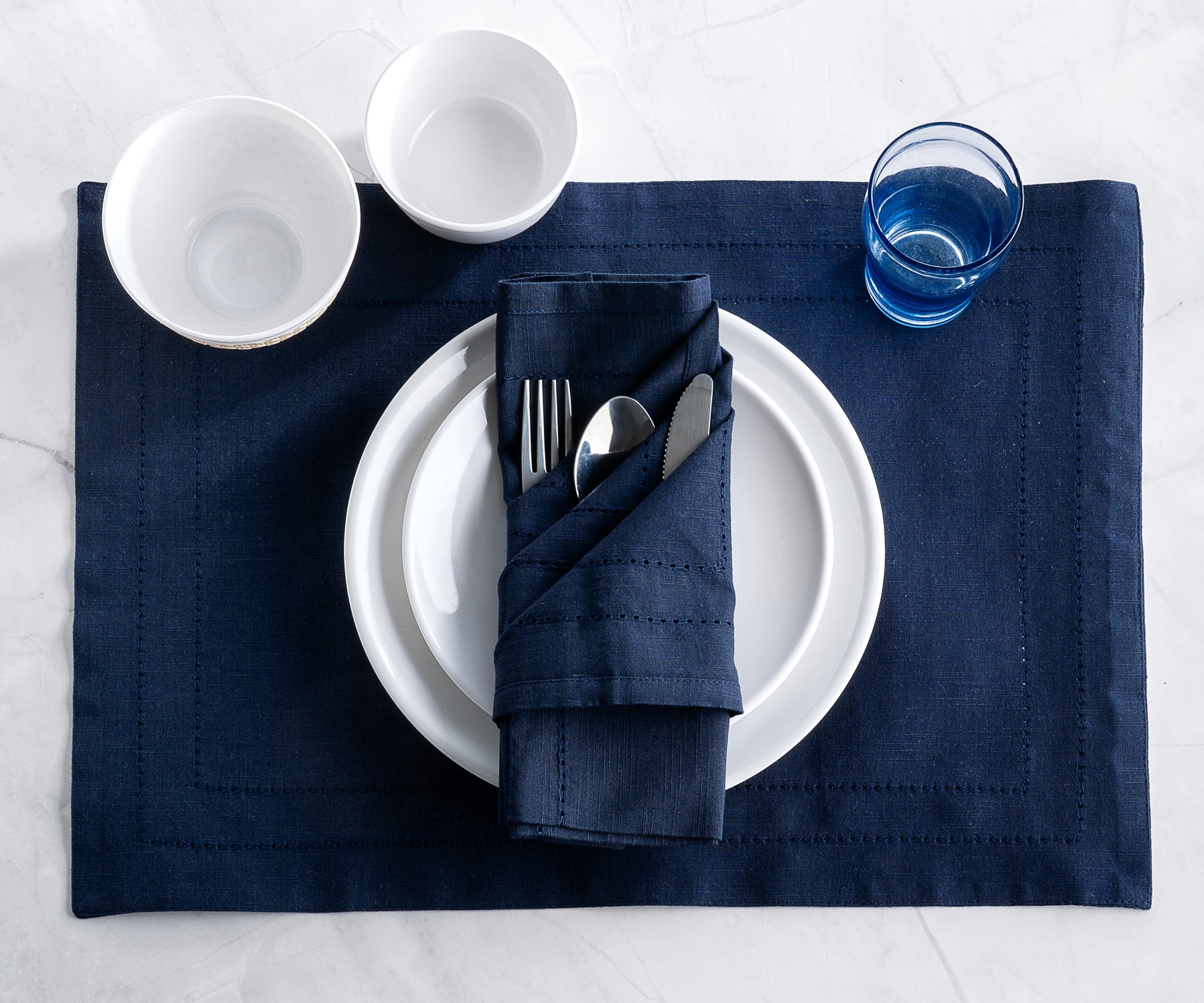 Navy blue linen placemat with matching napkin, set with white plate, silver cutlery, and glassware.