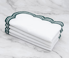 Set of white linen napkins featuring intricate green scalloped embroidery, ideal for upscale table decor.