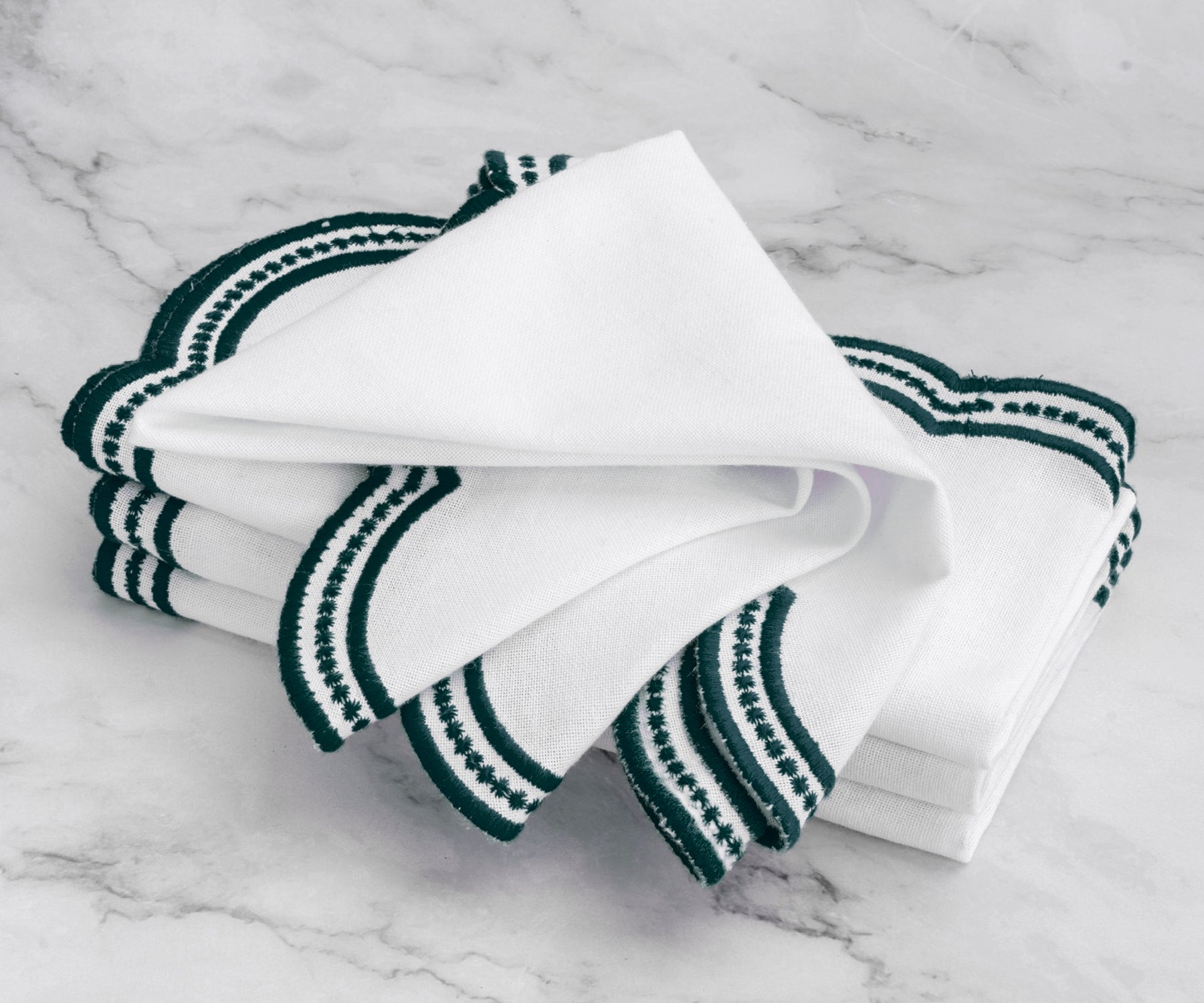 Classic embroidered napkins with green scalloped edges, adding sophistication to any dining arrangement.