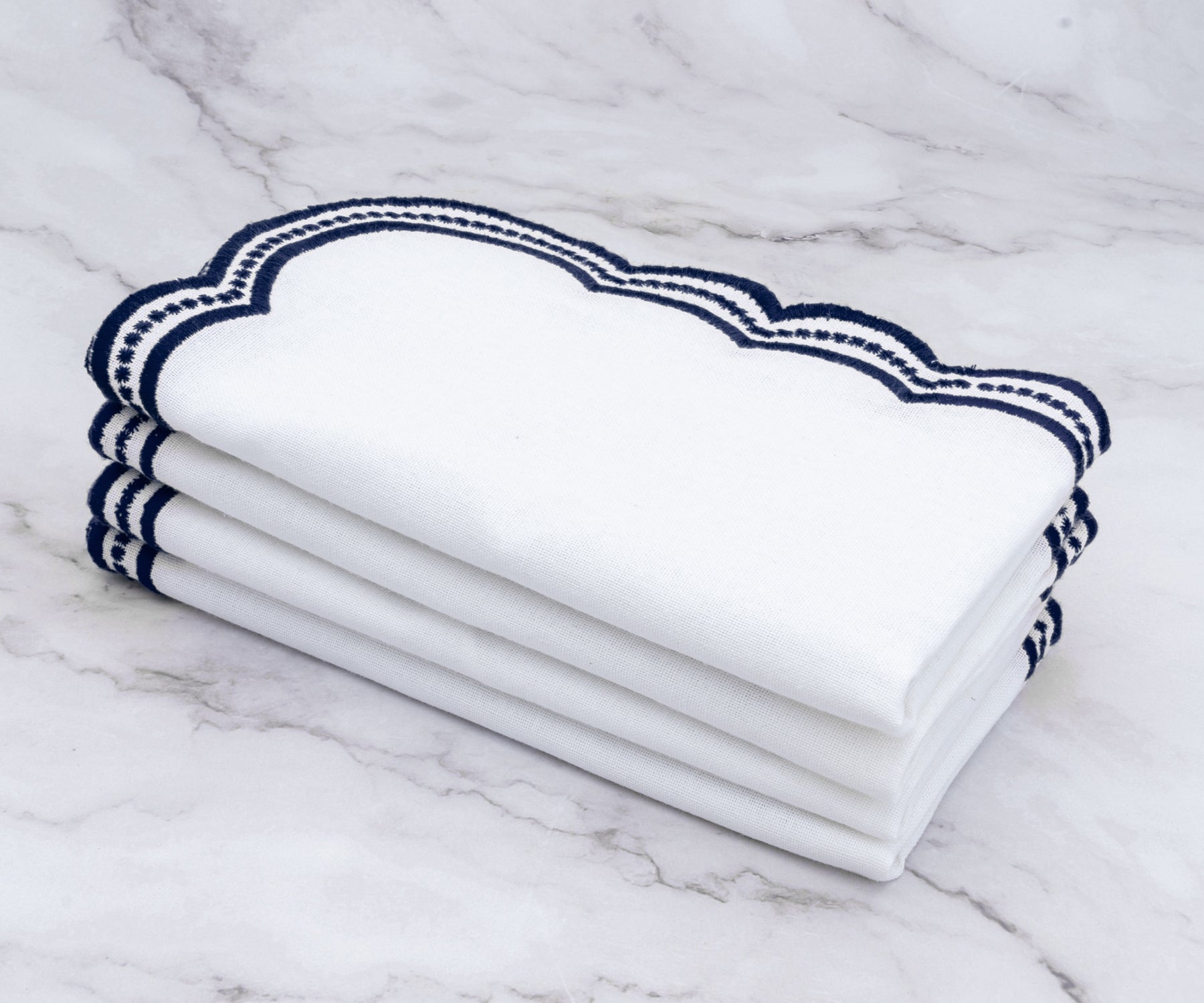 White linen napkins with navy blue scalloped embroidery, elegantly folded on a matching placemat.