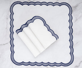 Set of white linen napkins with navy blue scalloped trim, folded and displayed on a matching placemat.