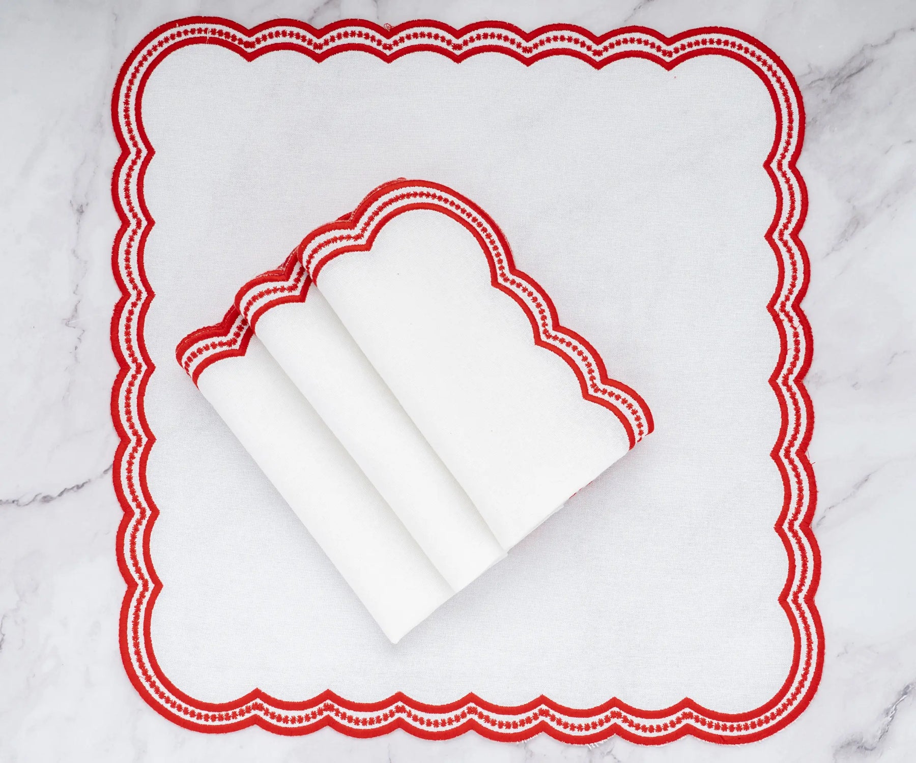 Classic embroidered napkins with red scalloped edges, enhancing table decor with a touch of elegance.