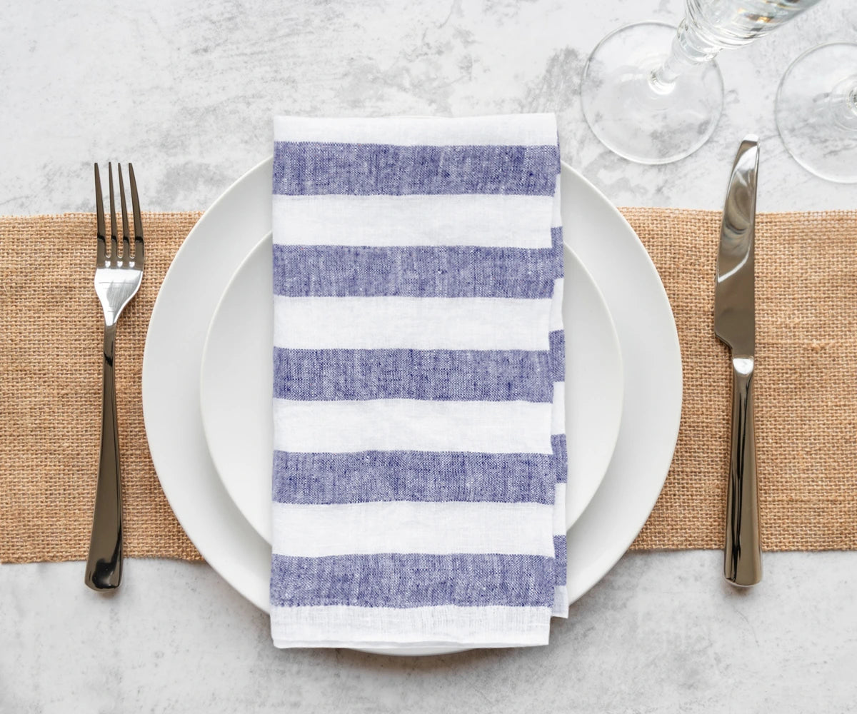 Elegant fancy linen napkins folded into intricate designs, placed next to fine cutlery on a formal dining table setting.