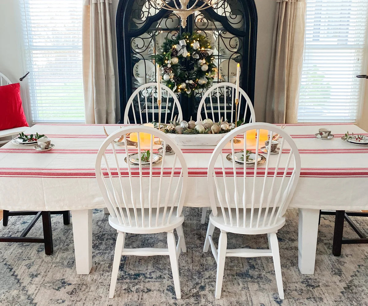 Dining table with a red and cream striped tablecloth, white chairs, and holiday decor.