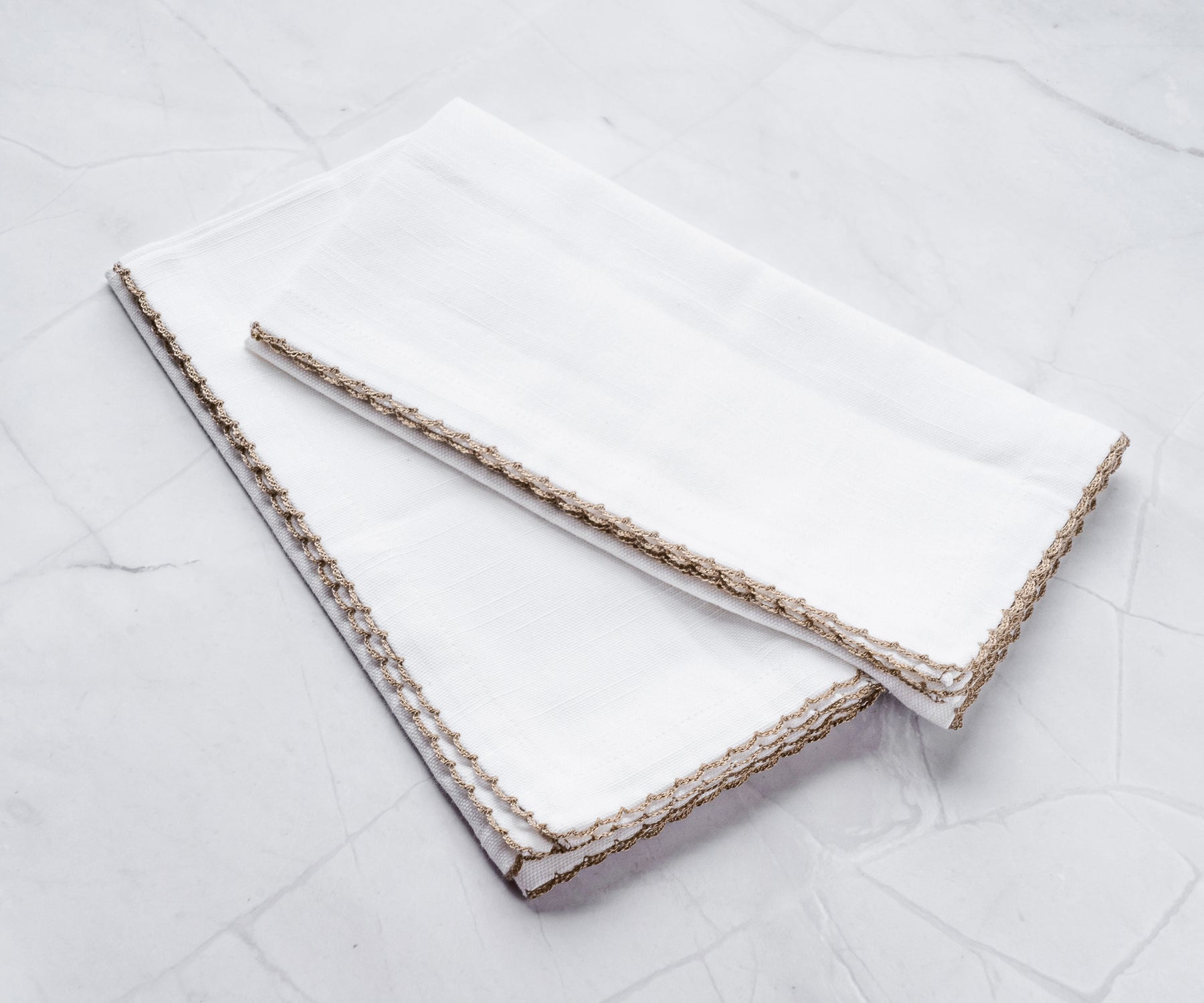 White napkins with beige edge bunting stitch, folded on marble.