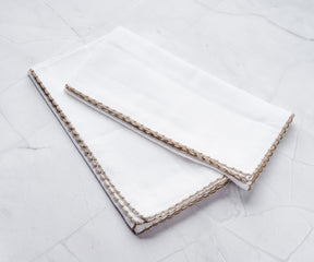 White napkins with beige edge bunting stitch, folded on marble.