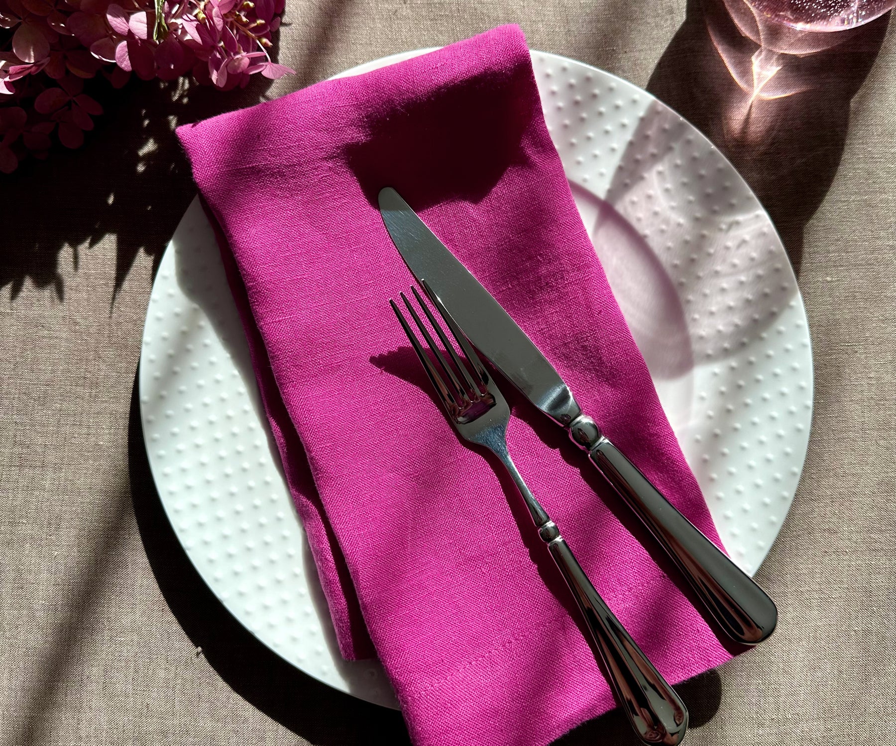 Elegant orchid linen plain dinner napkin styled on a white plate with green sage leaves.