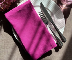 Dinner setting with an orchid plain linen napkin on a plate and sage leaves for detail.