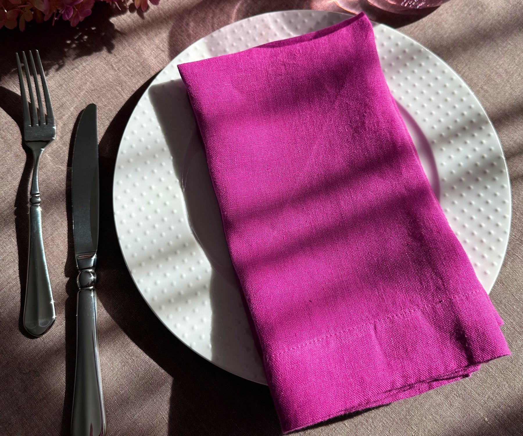 White plate featuring an orchid linen plain dinner napkin and a small bundle of sage leaves.