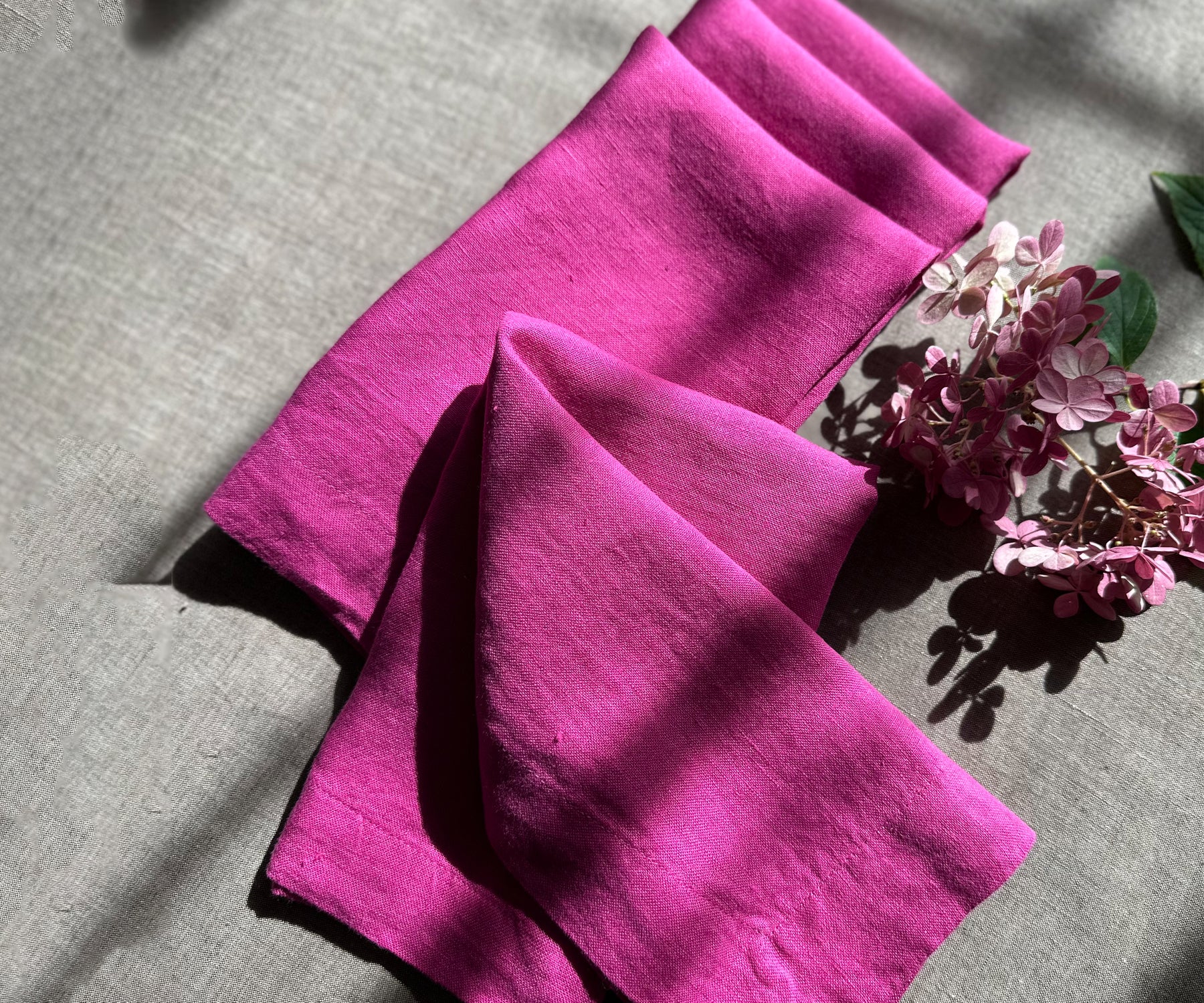 Flat lay of an orchid linen dinner napkin with sage leaves on a white ceramic plate.