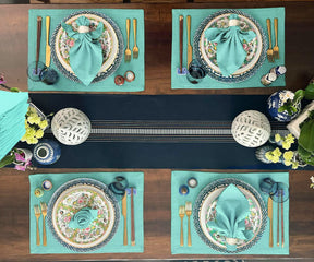 Table setting featuring a light blue napkin, ceramic plate, and artistic tablecloth design.