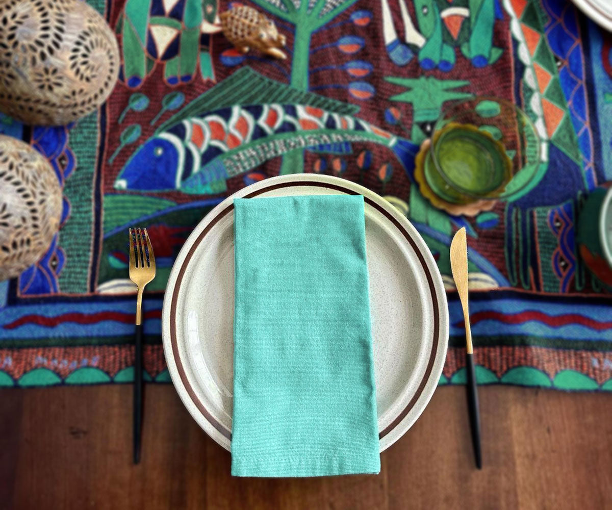 Tonal light blue napkin on a dinner plate, paired with gold cutlery and vibrant decor.